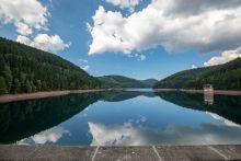 von dem Staudamm aus im Anschnitt ist die wasserfläche mit darin stehenden Wasserentnahmeturm zu sehen. links und rechts die Ufer sind bewaldet