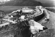 historische Aufnahme, Gerüst zur Errichtung des Damms und teilweise errichteter Damm mit Baumaschinen