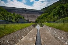 Der Fluss Lichte schlängelt sich vor der Staumauer, der rechte Hang ist bewaldet