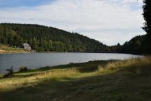 Im Anschnitt ist eine Wiesenfläche zu sehen mit Blick auf die Wasserfläche der Talsperre und am gegenüberliegenden Ufer ist ein Haus zu sehen.