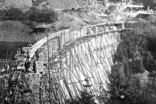 im Bau befindliche Staumauer mit Gerüst auf der Luftseite der Staumauer sowie die Arbeitenden sind auf der schwarz/weiß-Aufnahme