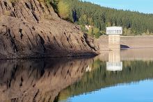 Blick auf den Stauraum der Talsperre mit geringem Füllstand, in der Mitte ist der Entnahmeturm zu sehen, der weit aus dem Wasser herausragt. Links sind die langen Hänge sichtbar.