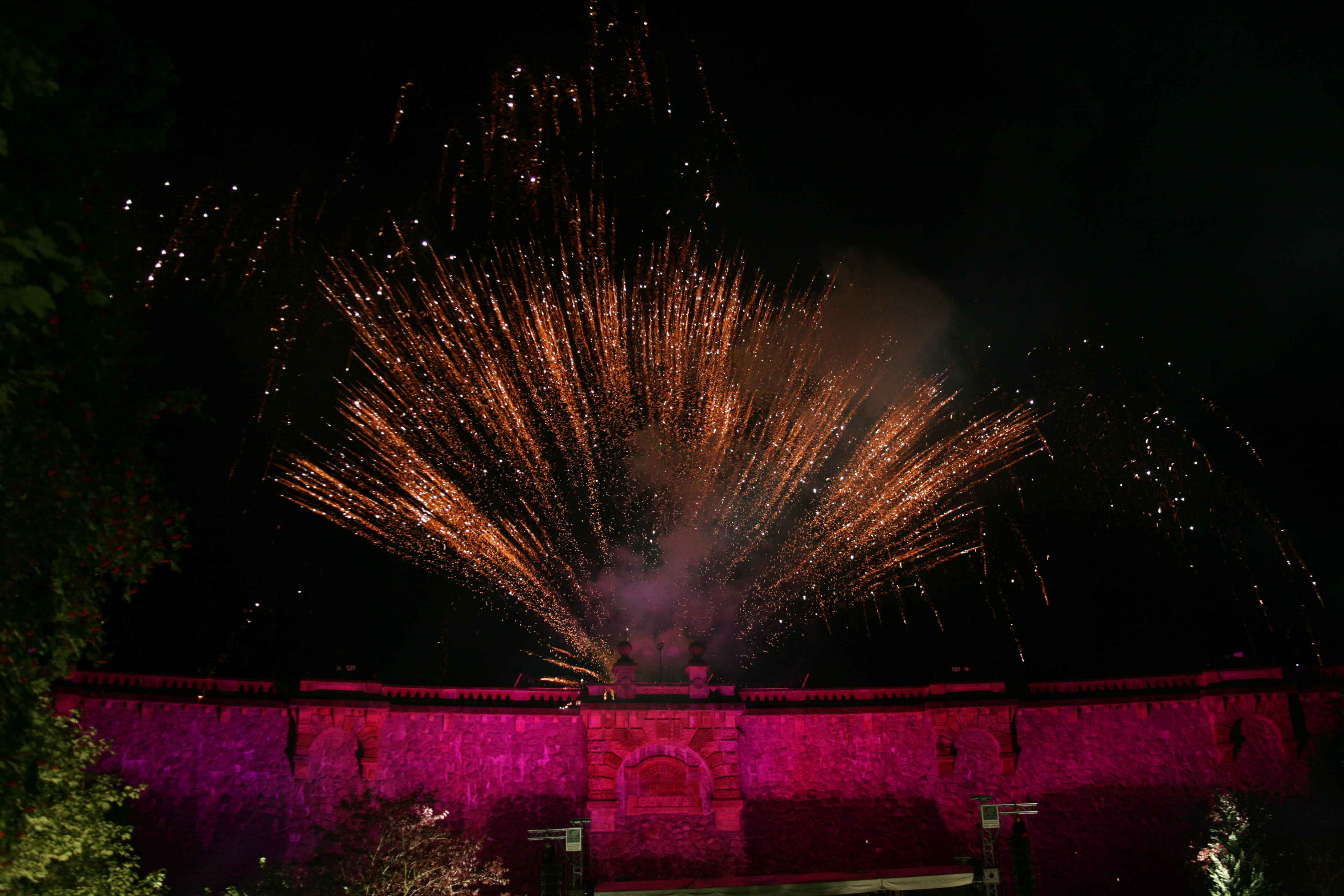 Feuerwerk über der in rotes Scheinwerferlicht getauchten Staumauer der Talsperre
