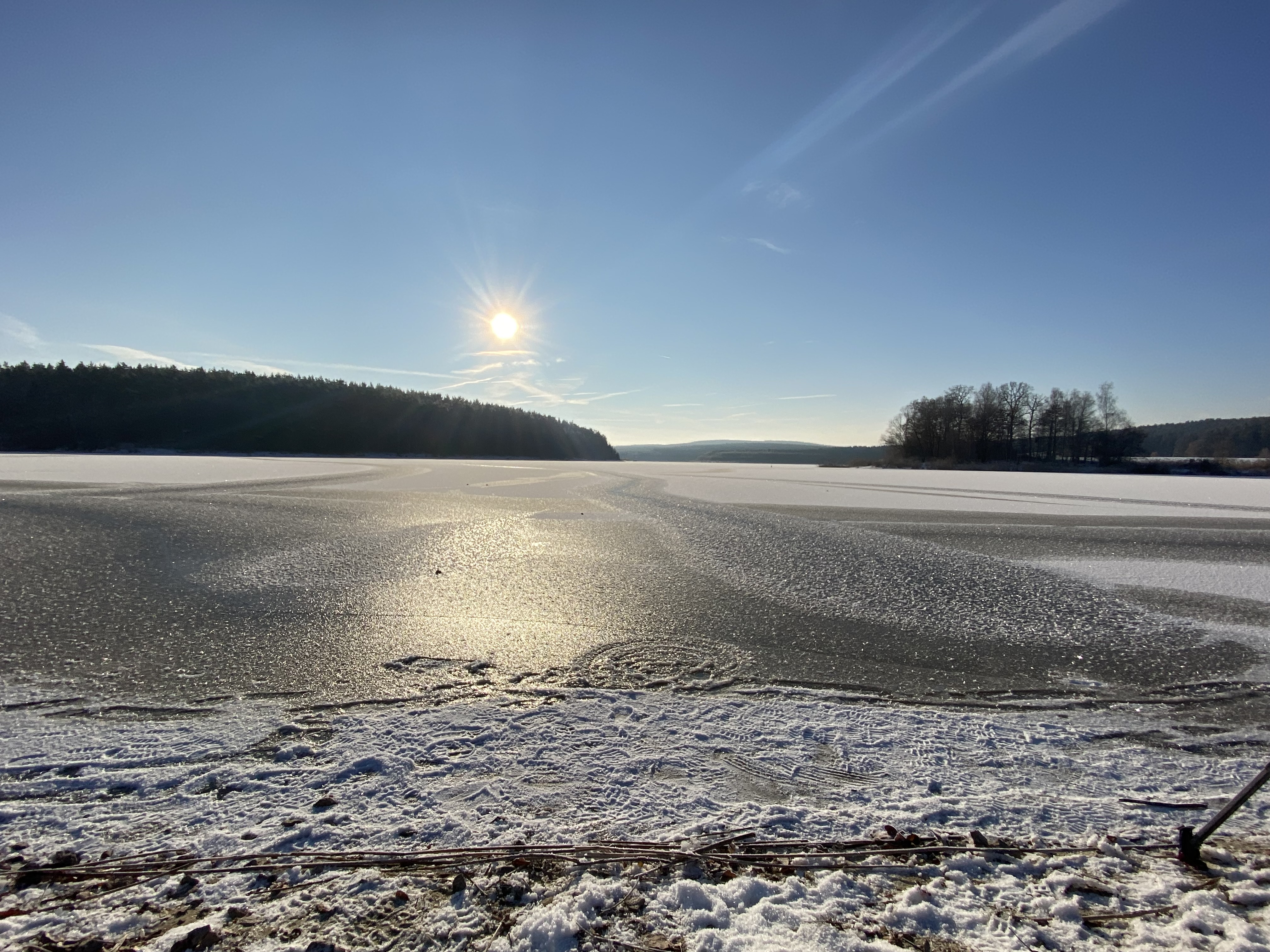 Eine dünne Eisschicht bedeckt den Stausee der Talsperre Heyda an einem sonnigen Tag.