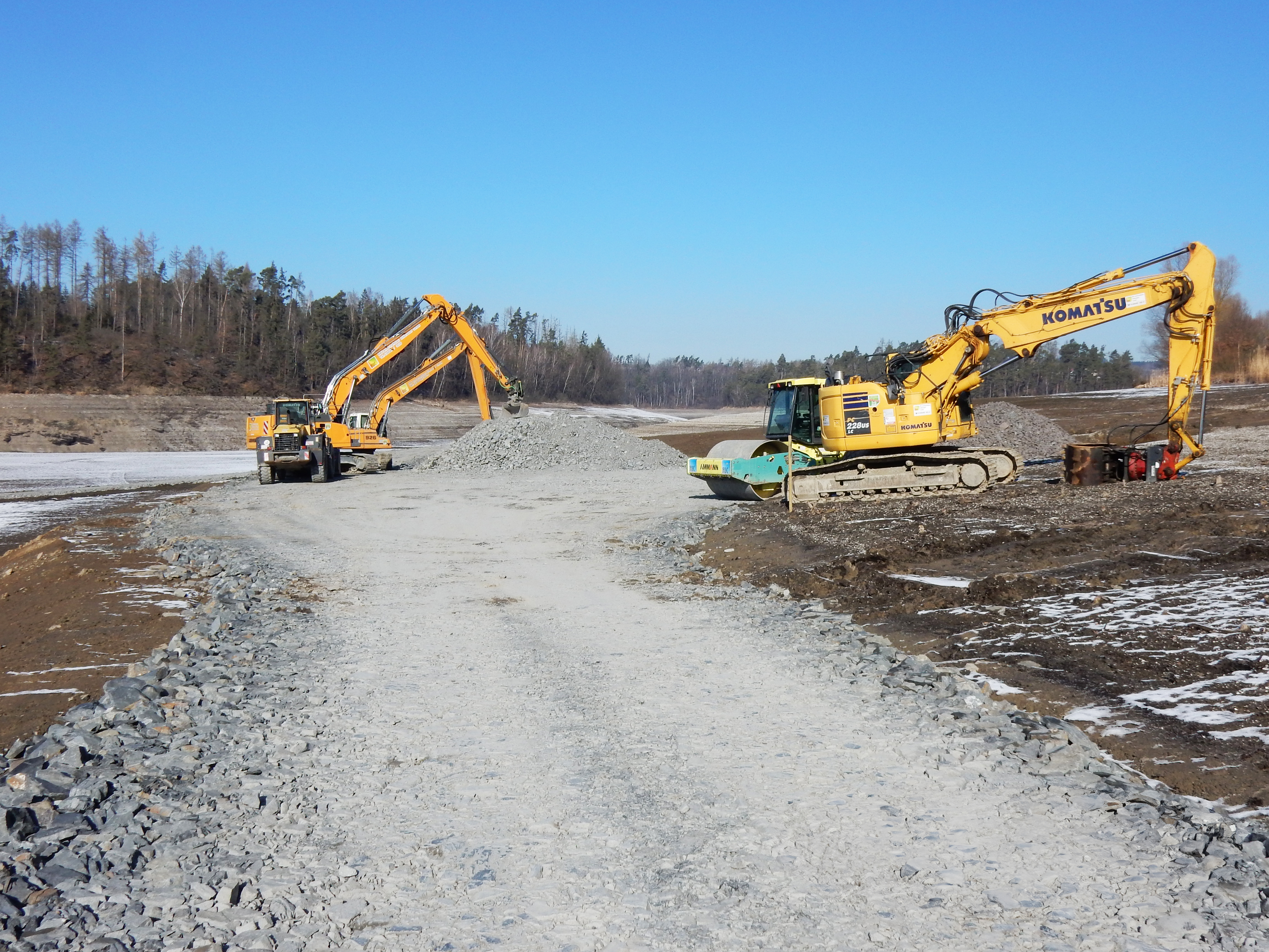Bagger schieben das Material für die neue Baustellenzufahrt im trockenen Staubecken.
