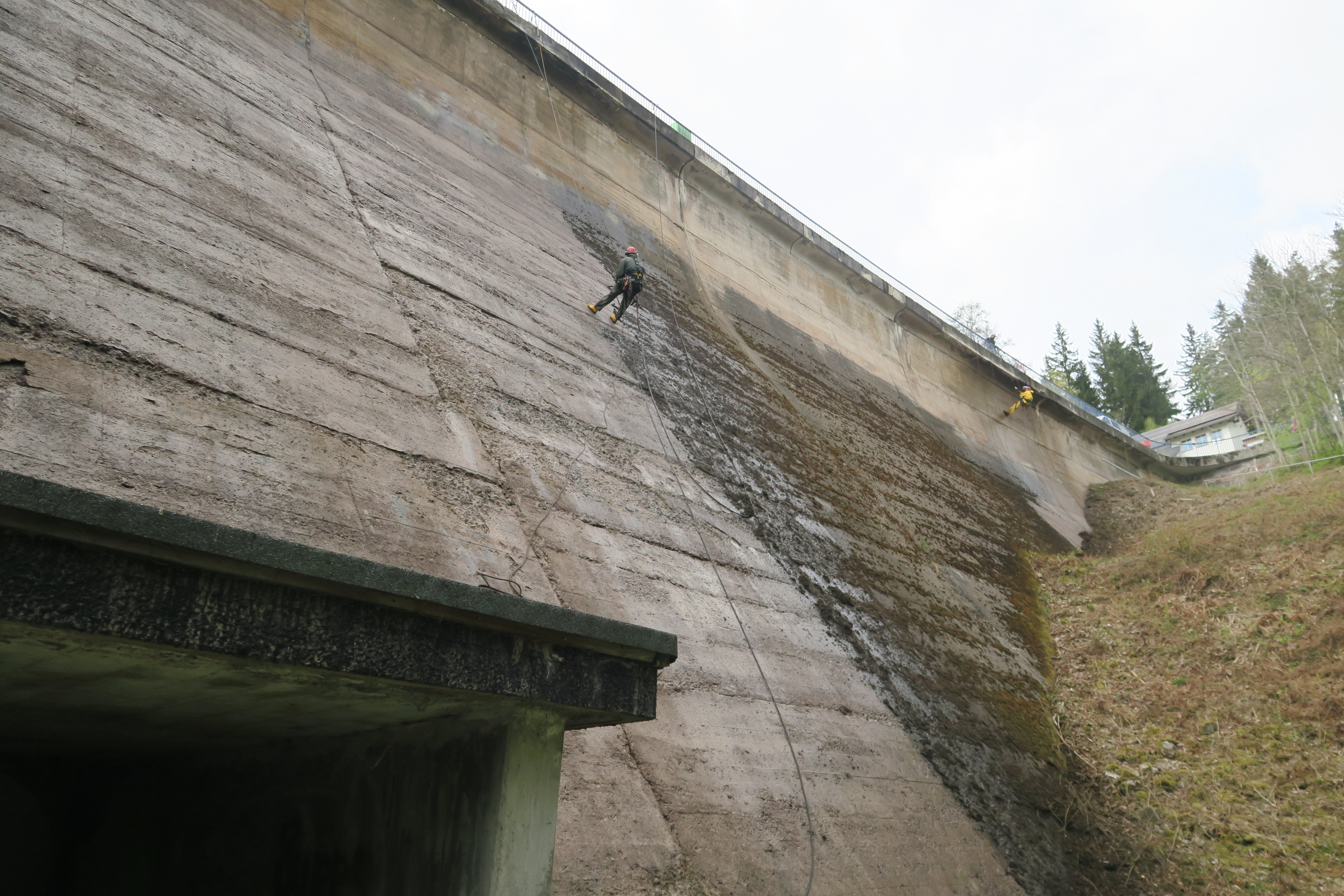 Industriekletterer seilen sich an der Staumauer ab und reinigen sie.