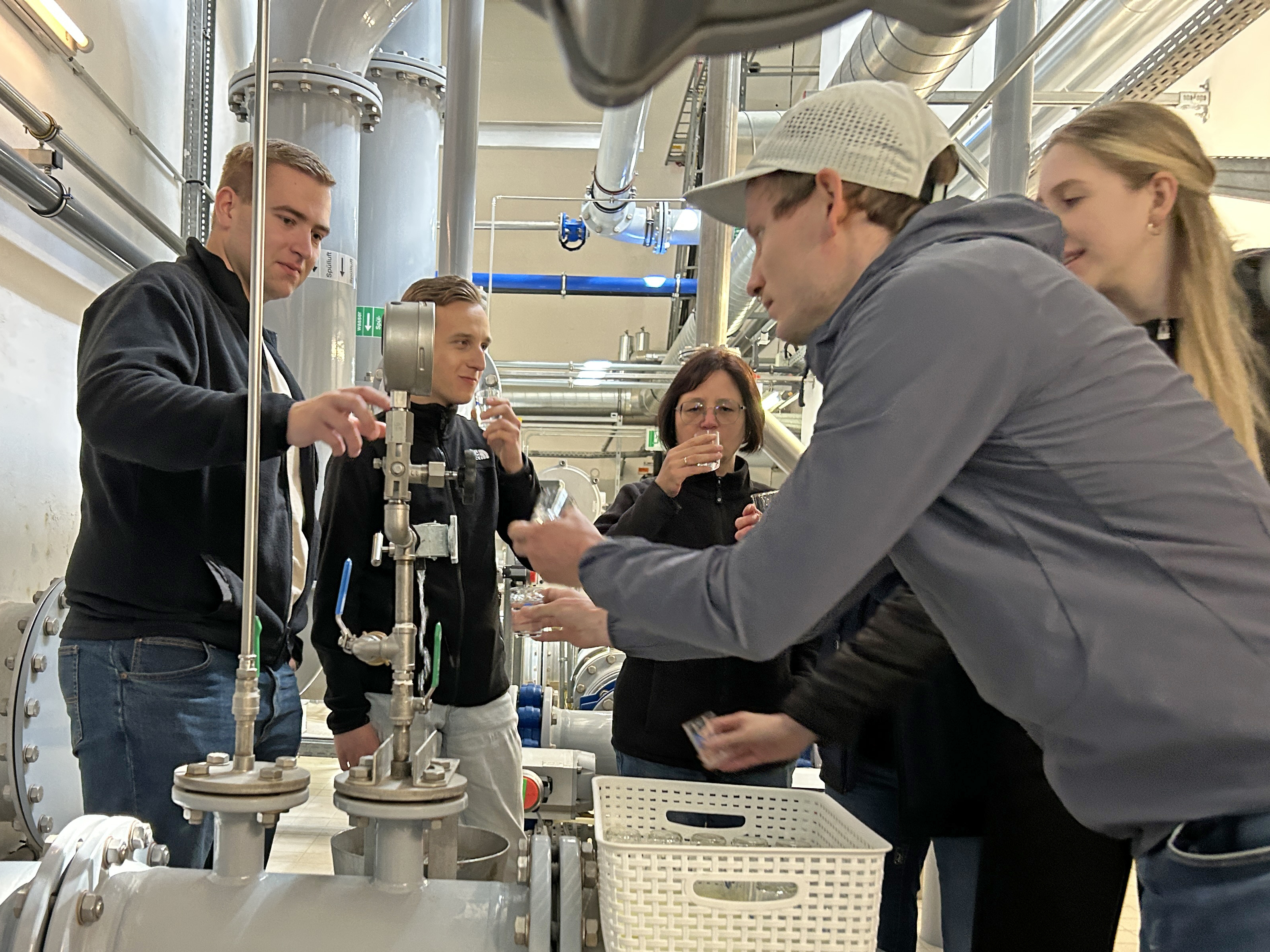 fünf Studierende stehen um den Zapfhahn im Wasserwerk udn verkosten das Wasser in kleinen Bechern