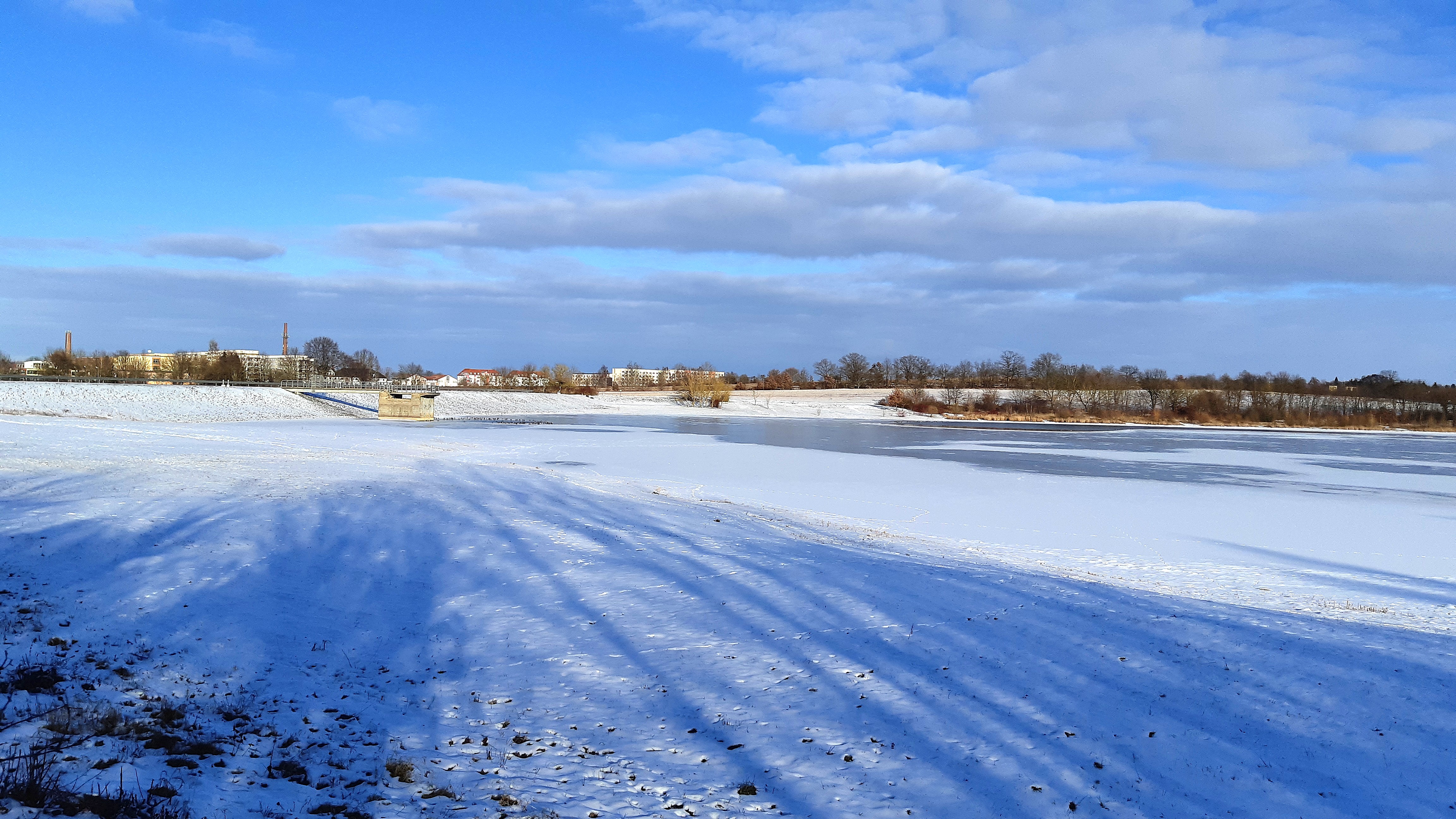 zugefrorene Talsperre Triptis, zum Teil mit Schnee bedeckt, am Horizont sind der Staudamm und das Abschlussbauwerk sowie leichter Bewuchs mit Bäumen
