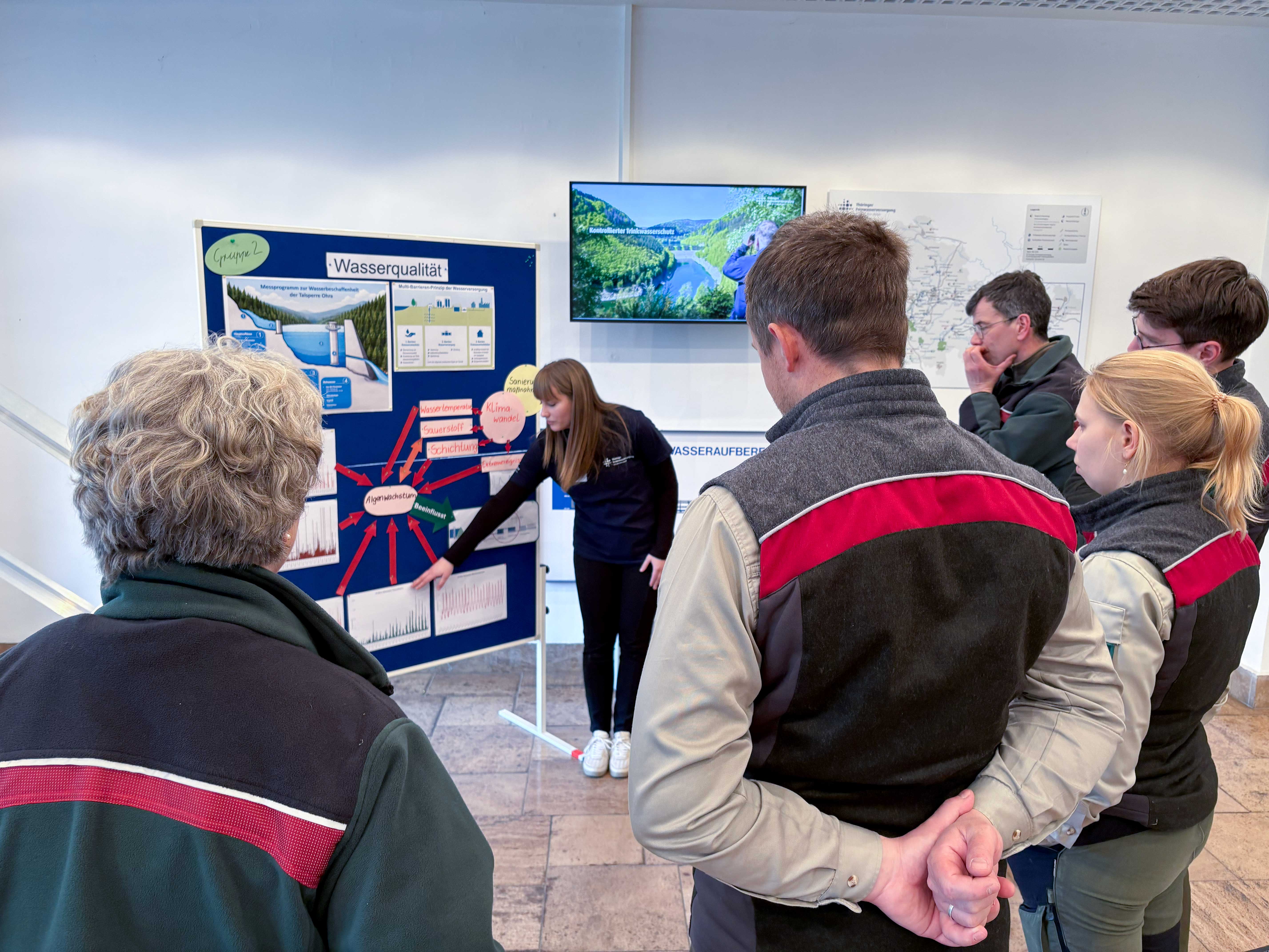 Eine Mitarbeiterin der Thüringer Fernwasserversorgung steht an einer Tafel mit Bildern und Grafiken zum Thema "Wasserqualität". Ihren Ausführungen lauschen aufmerksam Mitarbeitende von Thüringen Forst.