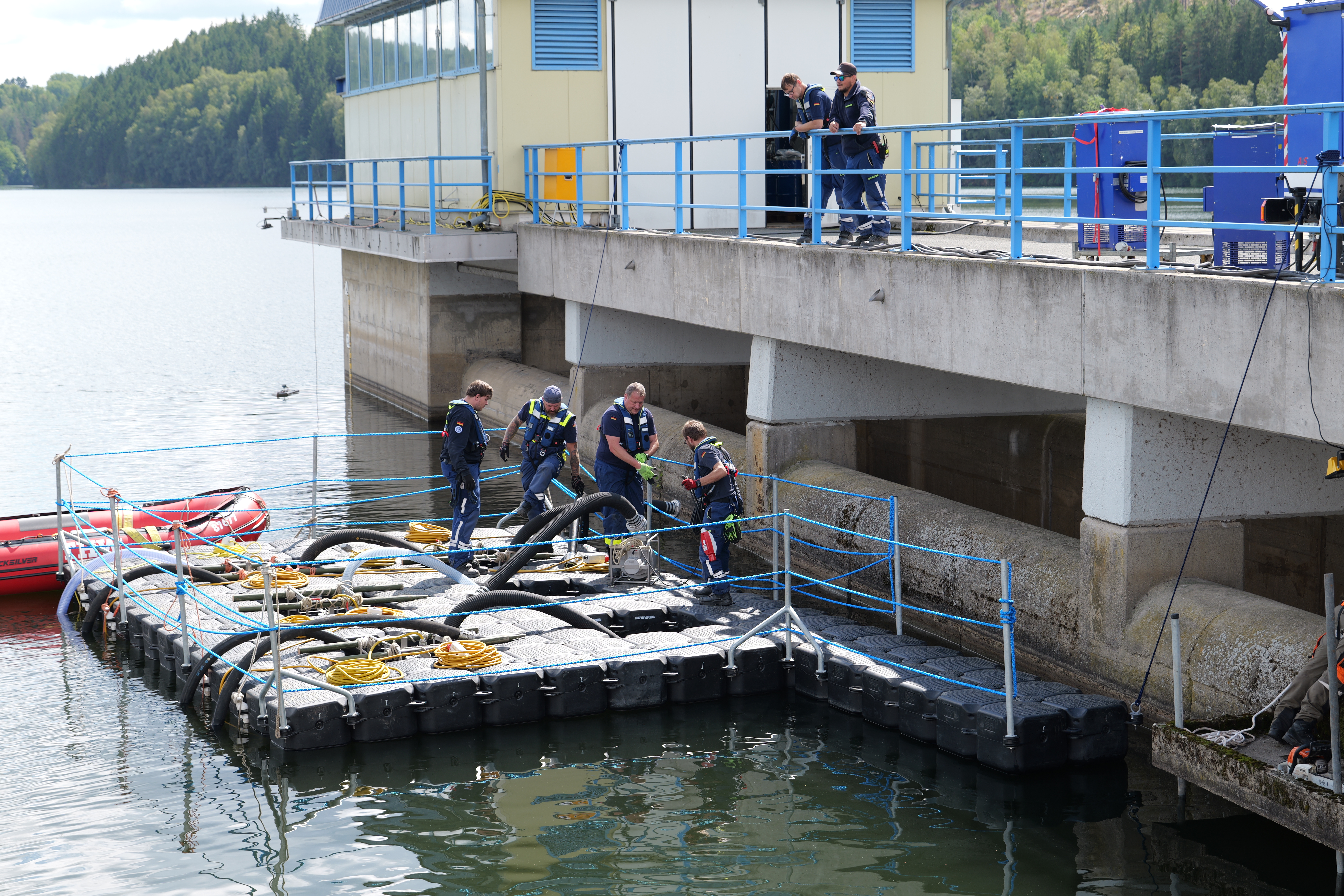 Ponton liegt an dem Bauwerk an, darauf sind einige Schläuche zu sehen und Helfer des THW, die die Technik installieren